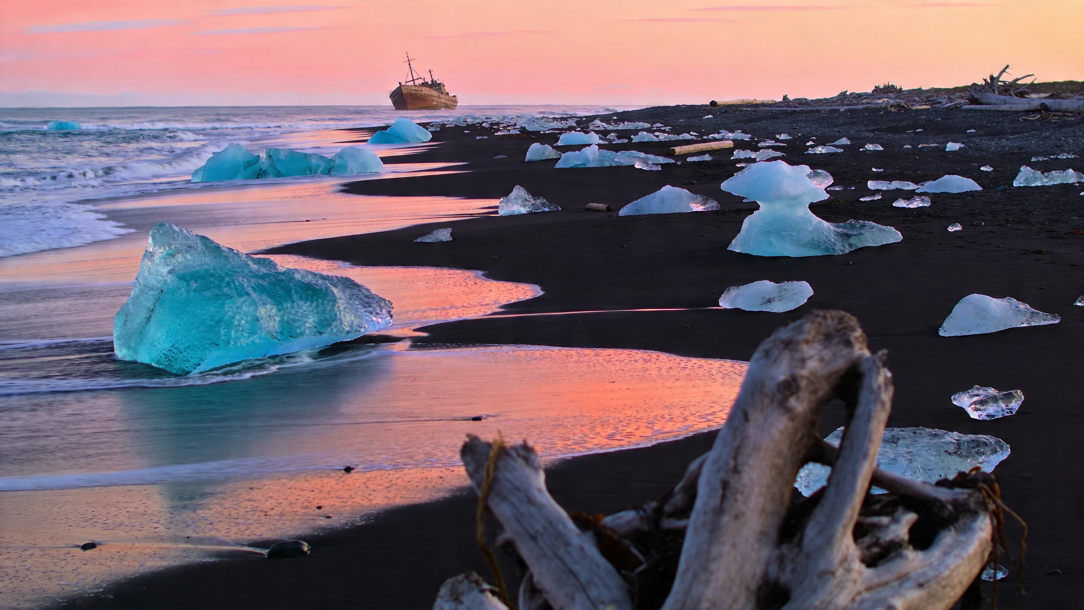 Aerial 4K photograph of an Icelandic black sand beach at sunrise, turquoise glacier chunks scattered across the volcanic sand, soft pink sky reflected in wet tidal patches, lone wooden shipwreck in the distance, zero people, documentary landscape photography, National Geographic style, razor-sharp detail